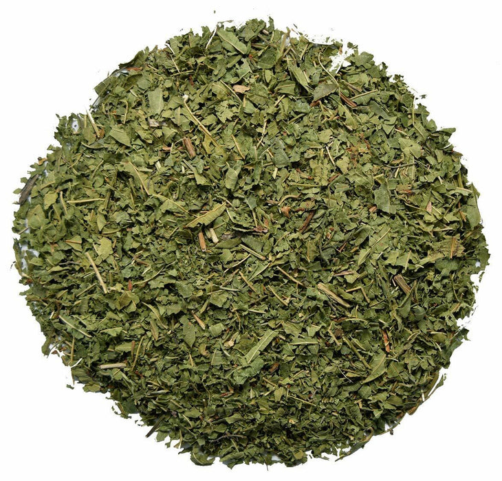Gros plan des feuilles séchées de verveine citronnée dans un bol blanc sur fond de bois coloré.