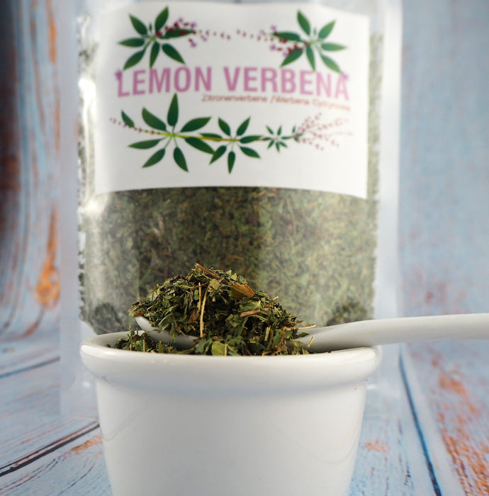 Infusion de thé de verveine citronnée dans une tasse transparente, accompagnée d'une cuillère dorée sur une table en bois.