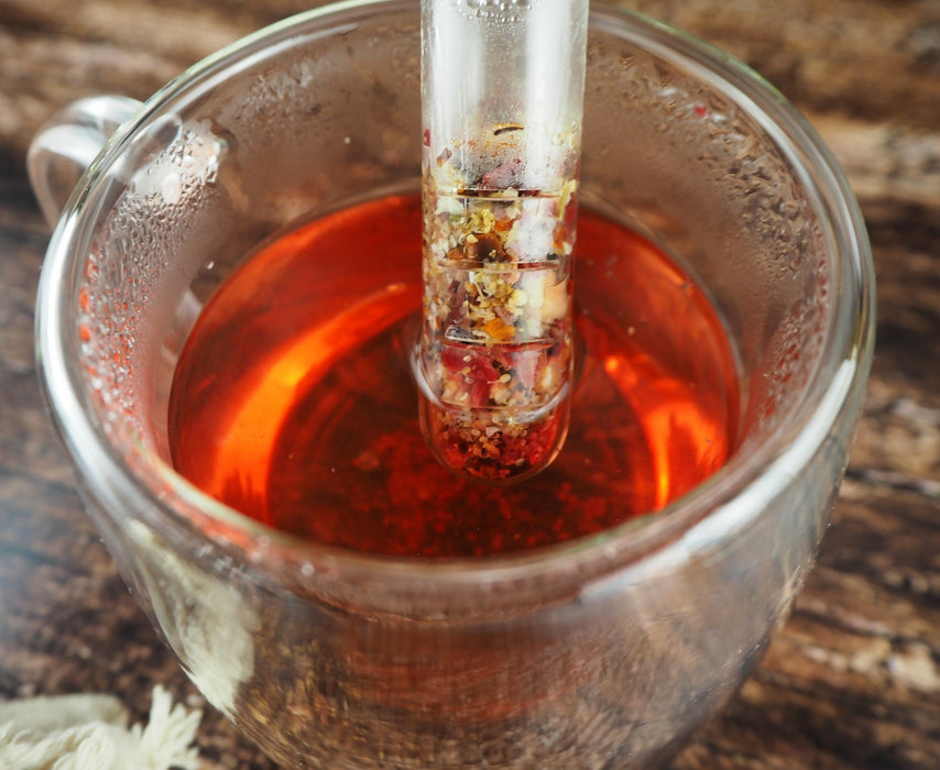 Infusion de thé rouge éclatante versée dans une tasse transparente, montrant la richesse des ingrédients.