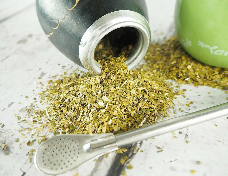 Yerba Mate brésilienne versée d'une calebasse traditionnelle à côté d'une cuillère à maté, prête pour la préparation d'une infusion revigorante.