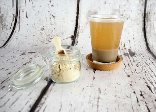 Infusion de poudre de calamus dans une tasse transparente à côté d'un bocal en verre avec cuillère en bois, pour une santé optimisée.