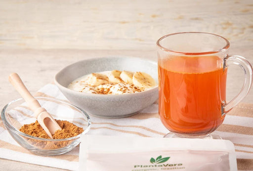 Un thé orange lumineux à côté d'un bol de yaourt avec banane et poudre de baies d'églantier bio sur un fond en bois rustique.