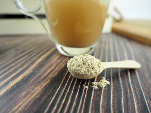 Cuillère de poudre de Ginseng de Sibérie avec un verre de thé en arrière-plan, sur une table en bois pour un mode de vie sain.