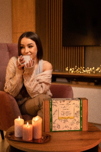 Jeune femme savourant une tasse de thé chaud, confortablement installée dans son salon avec un coffret cadeau à ses côtés.