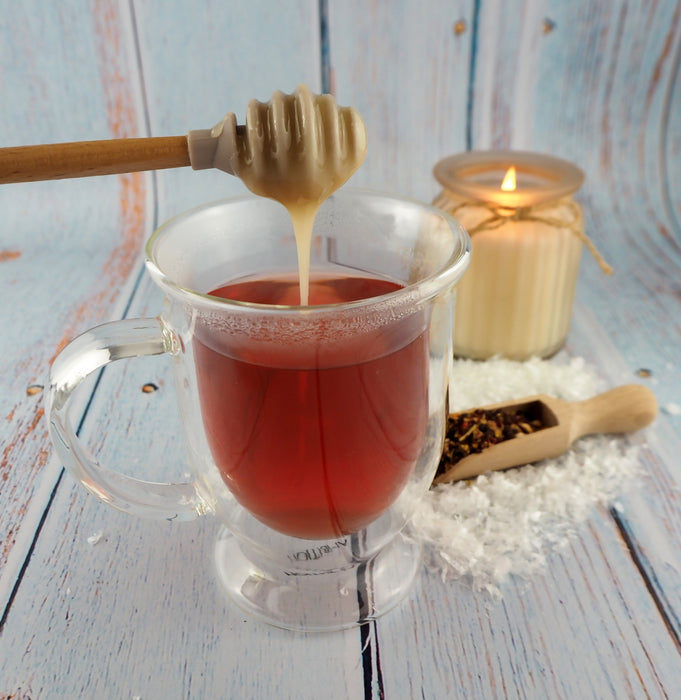 Miel coulant d'une cuillère dans une tasse de thé transparente, accompagnée d'une bougie allumée pour une pause douce.