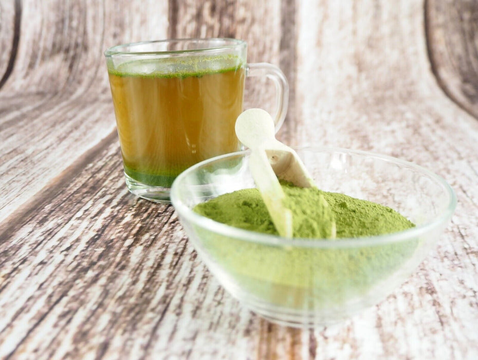 Poudre fine de feuilles de mûrier blanc en bol de verre à côté d'une tasse d'infusion.