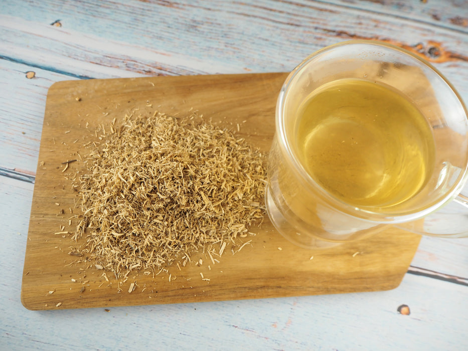 Planche en bois avec Racine de Taïga à côté d'une tasse de thé transparente, illustrant la préparation de thé de Ginseng Sibérien.