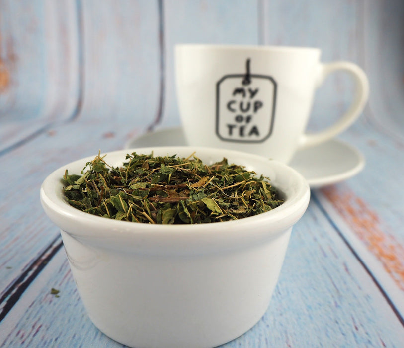 "Tasse blanche avec l'inscription 'My Cup of Tea' à côté d'un bol de thé de verveine citronnée sur fond bleu.