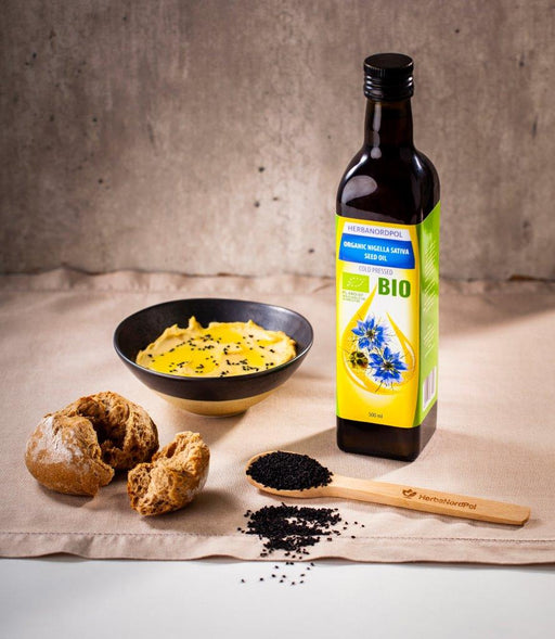Mise en scène d'huile de nigelle BIO avec pain et graines de Nigella sativa, invitant à un style de vie sain et naturel.