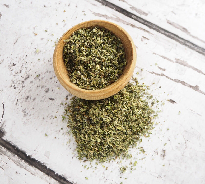 Infusion de feuilles de guimauve dans un bol en bois avec une tasse de thé vert sur un fond texturé blanc.