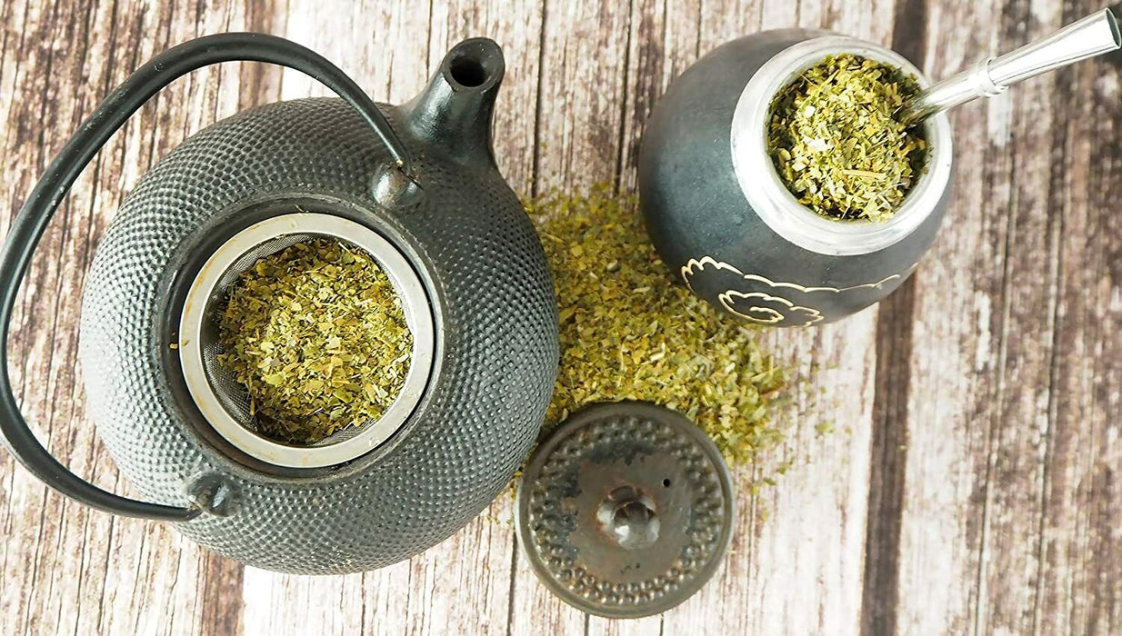 Théière moderne noire remplie de Yerba Mate désamargée et calebasse traditionnelle avec bombilla sur fond en bois.