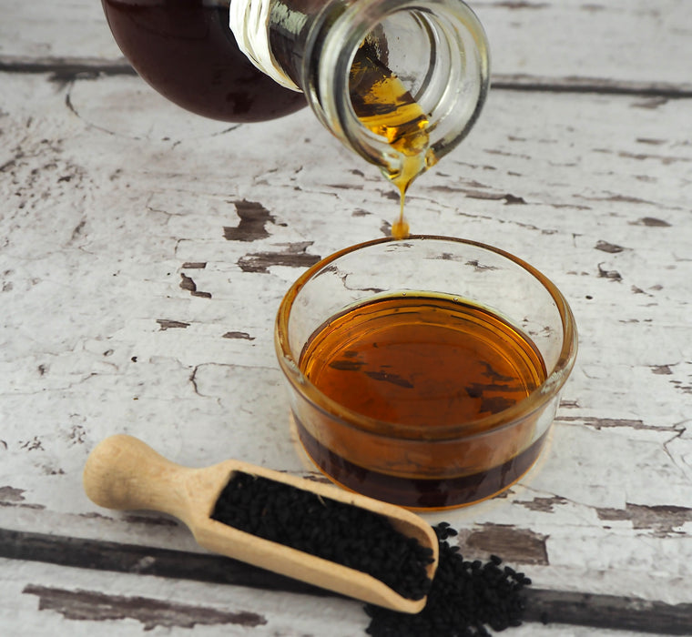 Versage d'huile de nigelle biologique dans un verre transparent sur fond rustique, accompagnée de graines de nigelle.