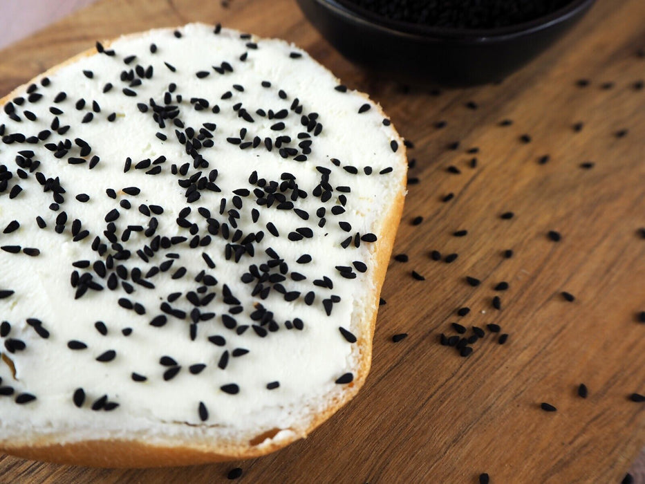 Tartine croustillante recouverte de graines de Nigelle noire BIO, créant un contraste appétissant sur une planche en bois.