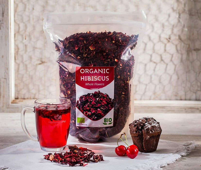 Présentation élégante d'un sachet de thé d'hibiscus bio avec une tasse d'infusion rouge et un muffin, invitant à la détente.