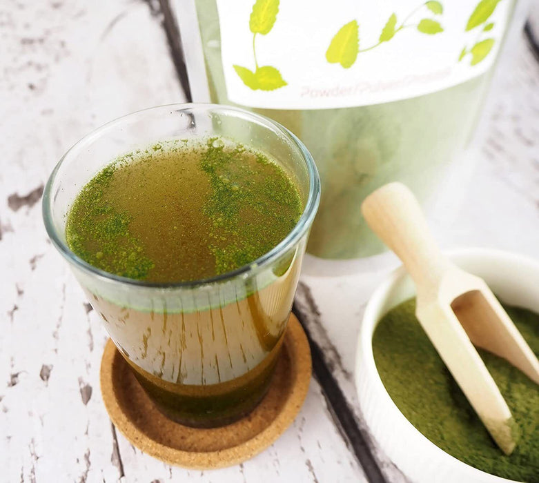 Infusion de poudre d'ortie biologique dans une tasse transparente, démontrant comment incorporer facilement ce super-aliment dans votre régime.