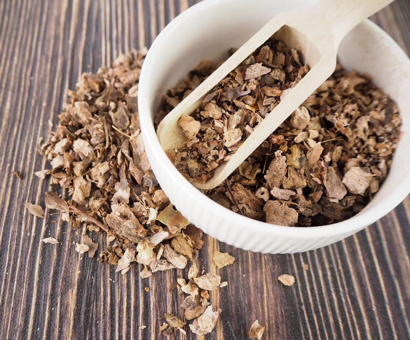 Bol blanc avec une cuillère en bois contenant de la Rhodiola Rosea séchée, vue en angle sur fond en bois.