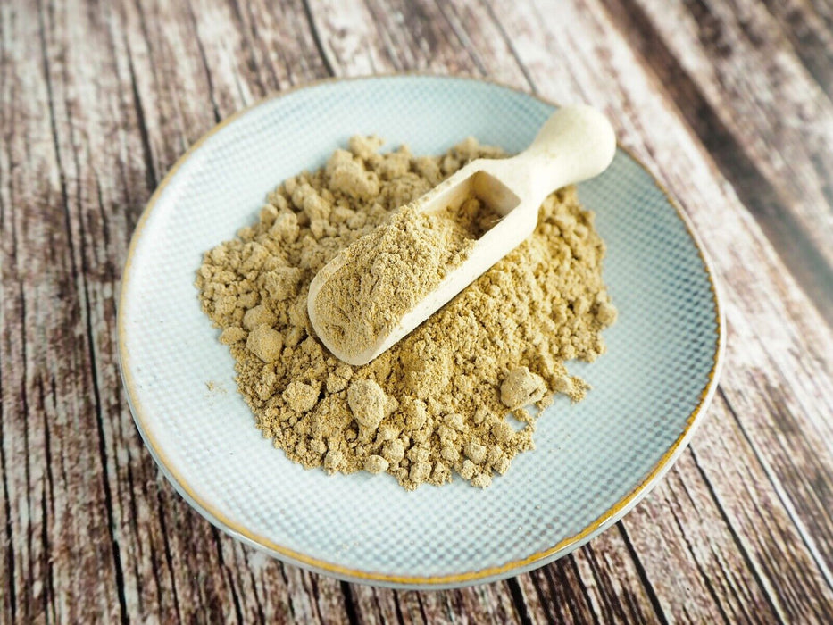 Assiette avec de la poudre de Chardon-Marie BIO et une cuillère en bois, prête pour l'ajout à des aliments.