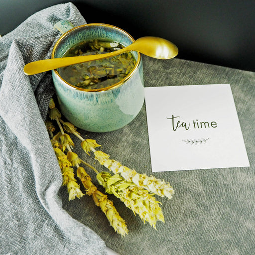 Moment de détente avec Thé des montagnes BIO Sideritis, tasse en céramique et cuillère dorée, accompagné d'un message 'tea time'.