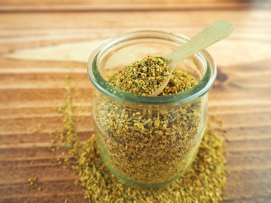 Bol en verre rempli de thé de fleurs de sureau séché, prêt à être infusé, sur un plan de travail en bois clair.