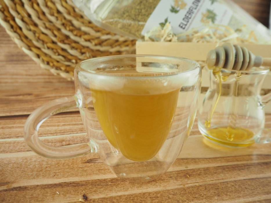 Une tasse de thé de fleurs de sureau transparente, accompagnée d'une tranche de citron et d'un biscuit, posée sur un fond rustique en bois.