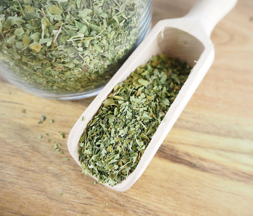 Feuilles de Moringa séchées et biologiques dans une cuillère en bois, sur un fond de bois rustique, suggérant une utilisation traditionnelle et authentique.