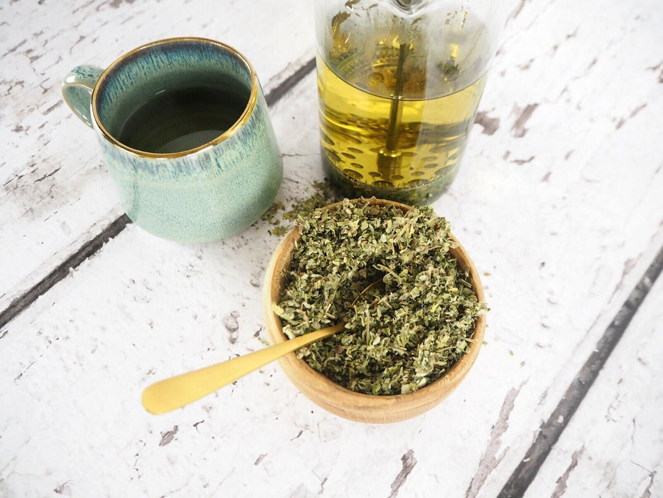 Tasse de thé en céramique verte à côté d'une carafe en verre avec infusion de feuilles de guimauve.