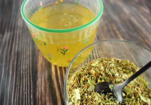 Infusion de fleurs de tilleul claire et apaisante dans une tasse colorée, avec des herbes à proximité sur une table en bois.