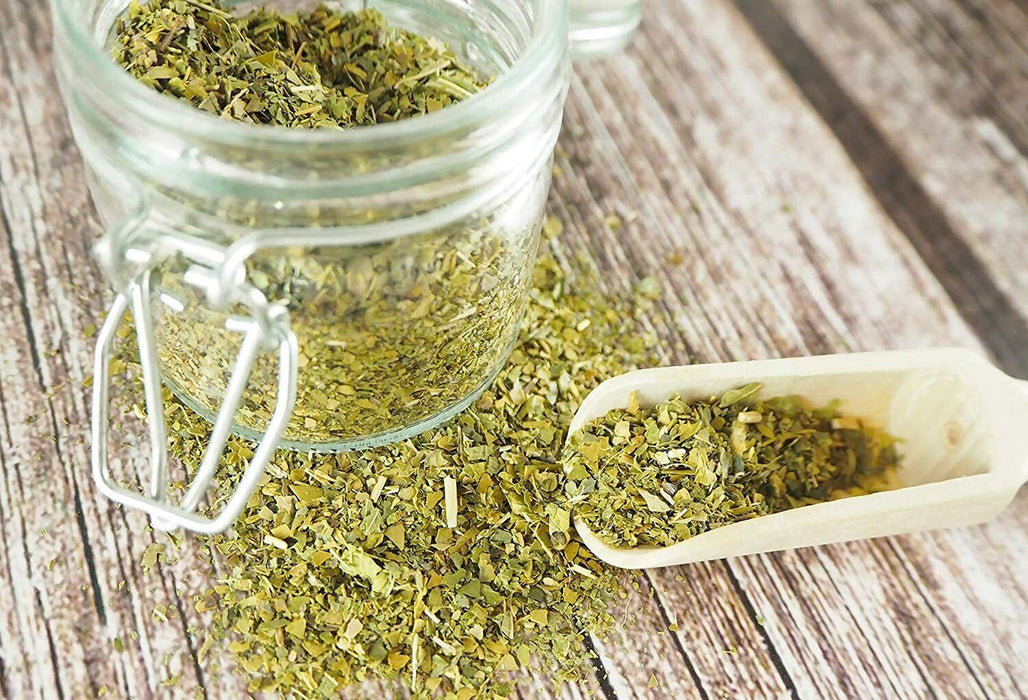 Yerba Mate désamargée avec verveine citronnelle présentée dans un bocal en verre ouvert à côté d'une cuillère en bois sur une table rustique.