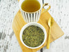 Thé infusé de feuilles de mûrier blanc dans une tasse élégante à rayures avec une cuillère dorée, sur un plateau en bambou.