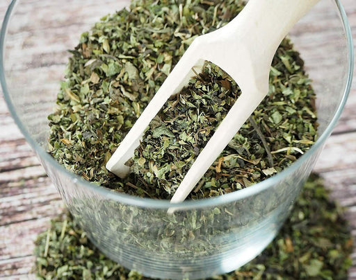 Cuvette en verre avec une pelle en bois contenant des feuilles séchées de Mélisse BIO Melissa Officinalis.